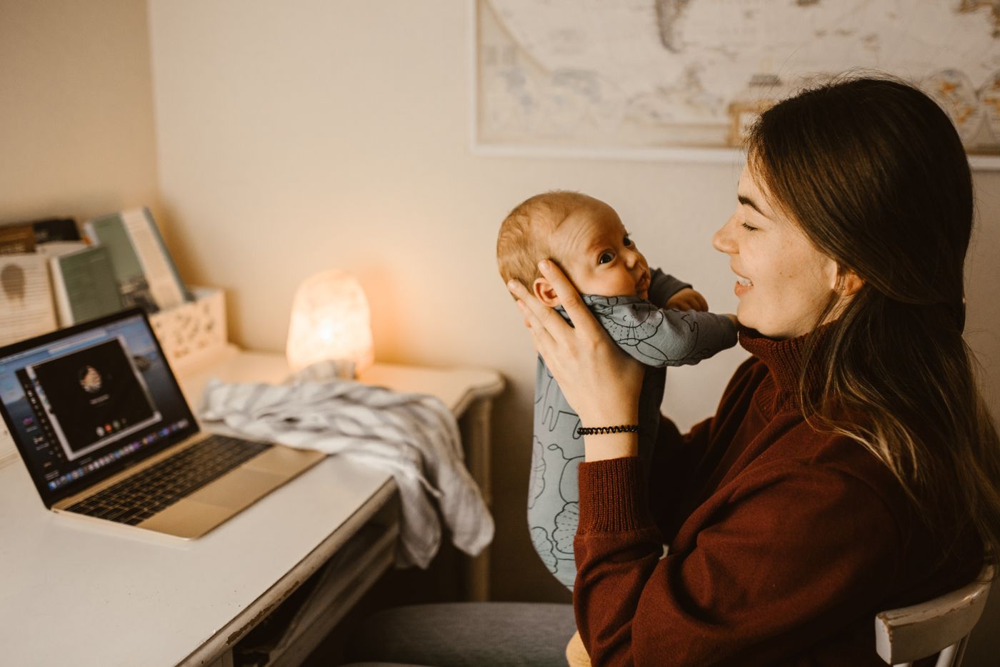 A mother cradling her newborn beside her laptop at home